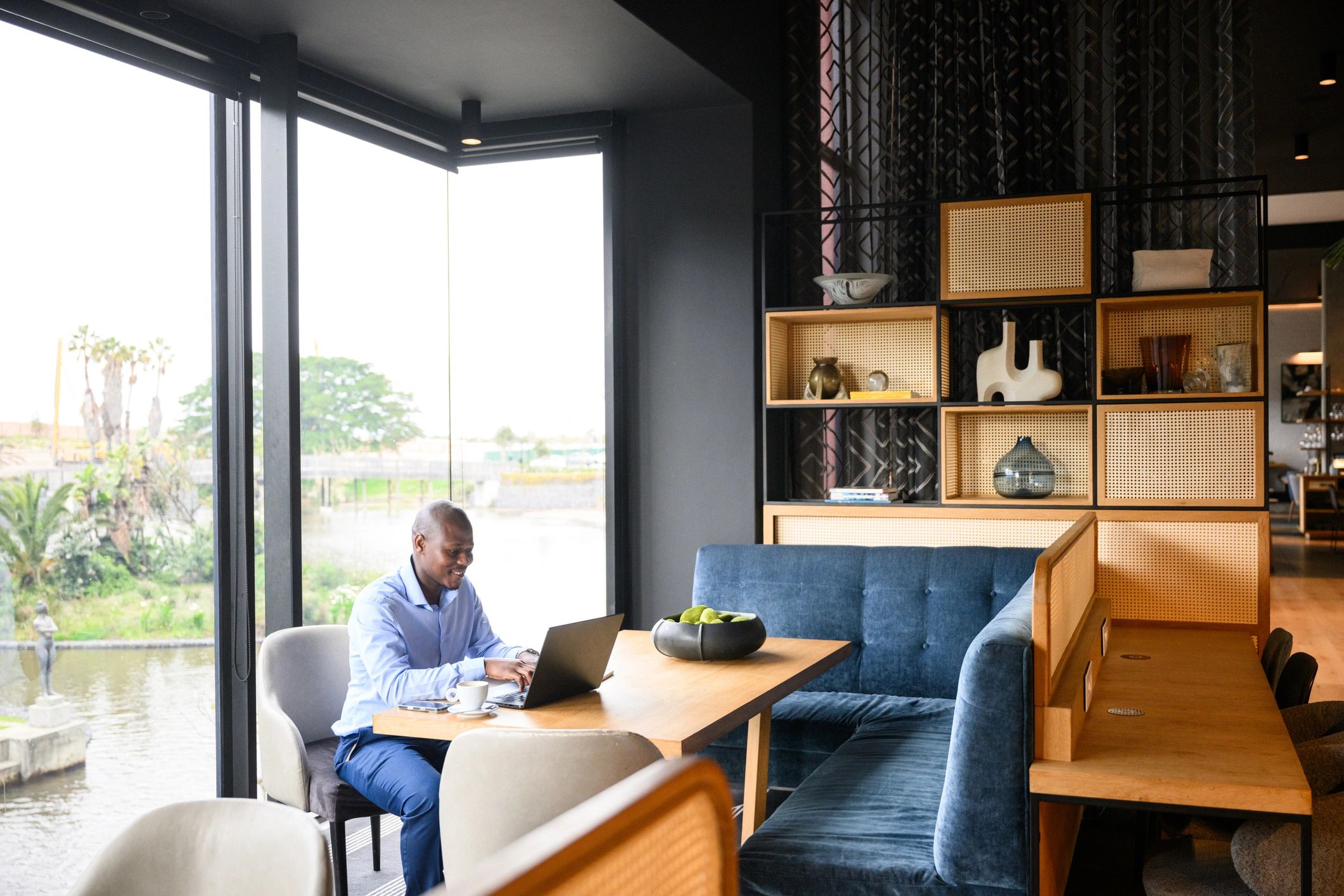 Wide shot of a businessman working on laptop in a contemporary office with large windows and stylish interior design